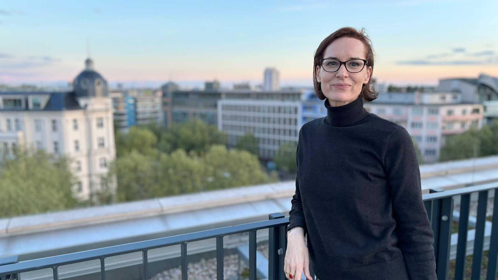Janina Unger auf einer Dachterrasse mit Blick über die Stadt im Abendlicht